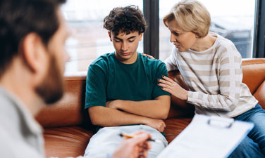 Portrait of sad woman calming her teenage son during psychiatrist session while psychologist writing notes. Counseling therapy. Psychology treatment.