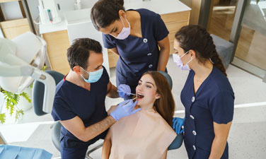 Male dentist wearing gloves and mask examining a patient teeth with a dental team in the clinic.