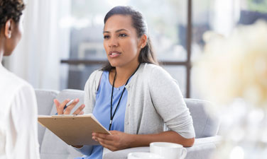 Confident African American female mental health professional gestures as she talks with an unrecognizable female patient.